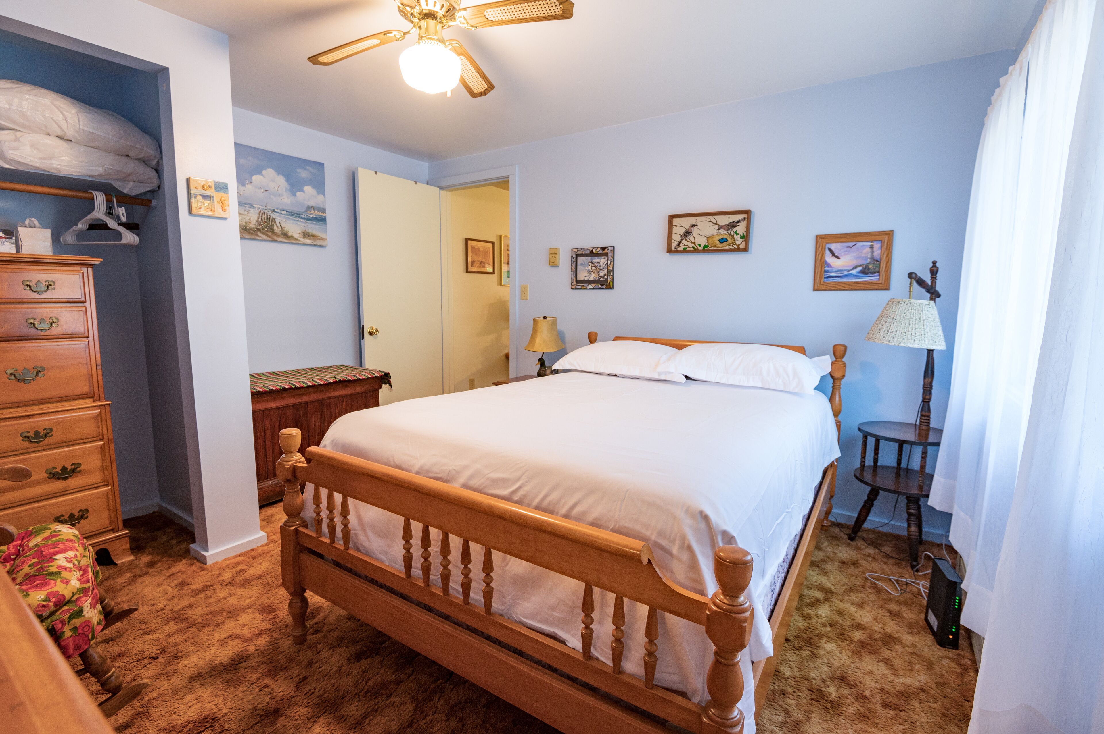 A bedroom with a wooden bed, a dresser, a ceiling fan, and wall art.