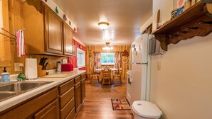 Una cocina con armarios de madera, un refrigerador, un lavamanos y un comedor con mesa y sillas.