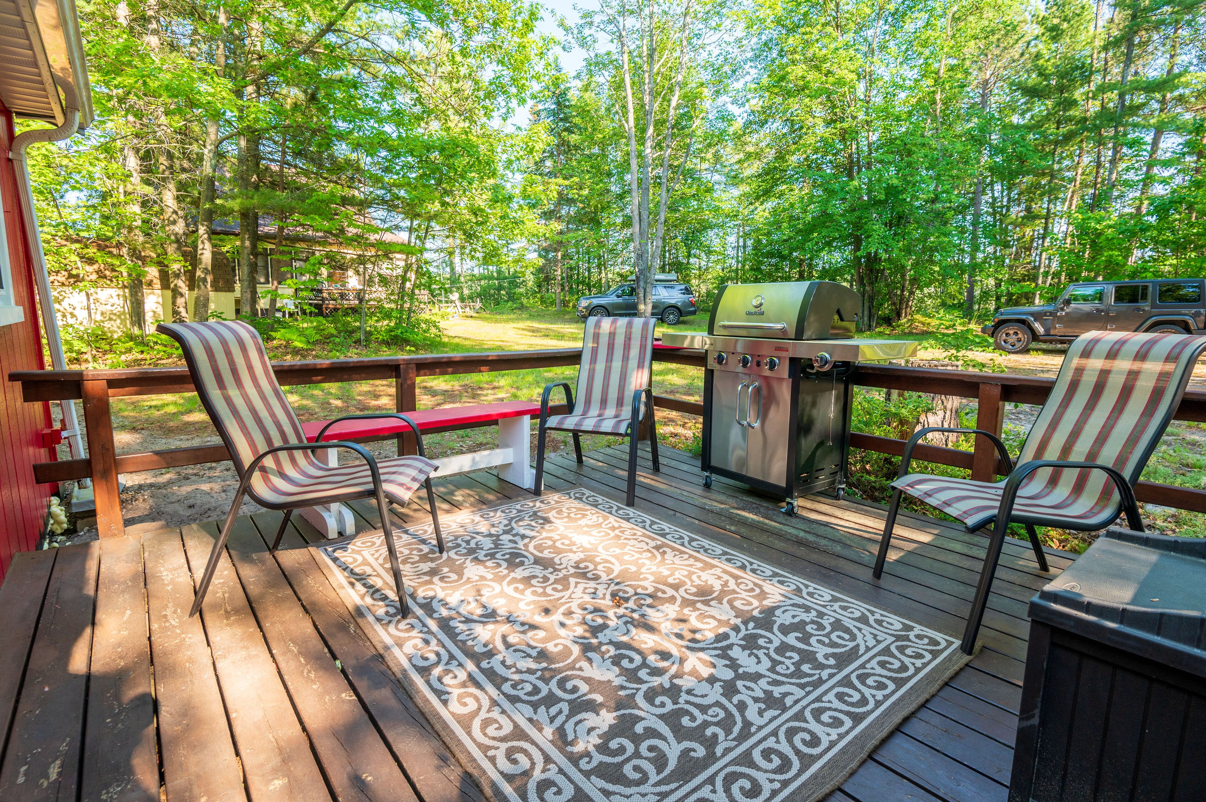 A wooden deck with a grill, chairs, and a rug.