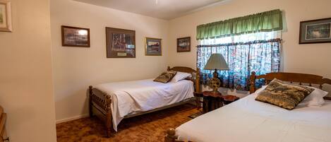 Un dormitorio con dos camas individuales, un ventilador de techo, una ventana con cortinas y cuadros en la pared.
