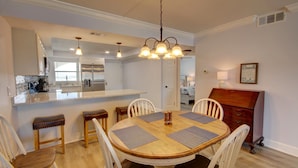 A dining area with a wooden table, white chairs, and a chandelier. - El Matador 461 -  FREE TICKETS!! Your stay includes free tickets to many area attractions! (Fort Walton Beach)