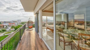 A balcony with a glass table and chairs, a hanging chair, and a view of the cityscape.