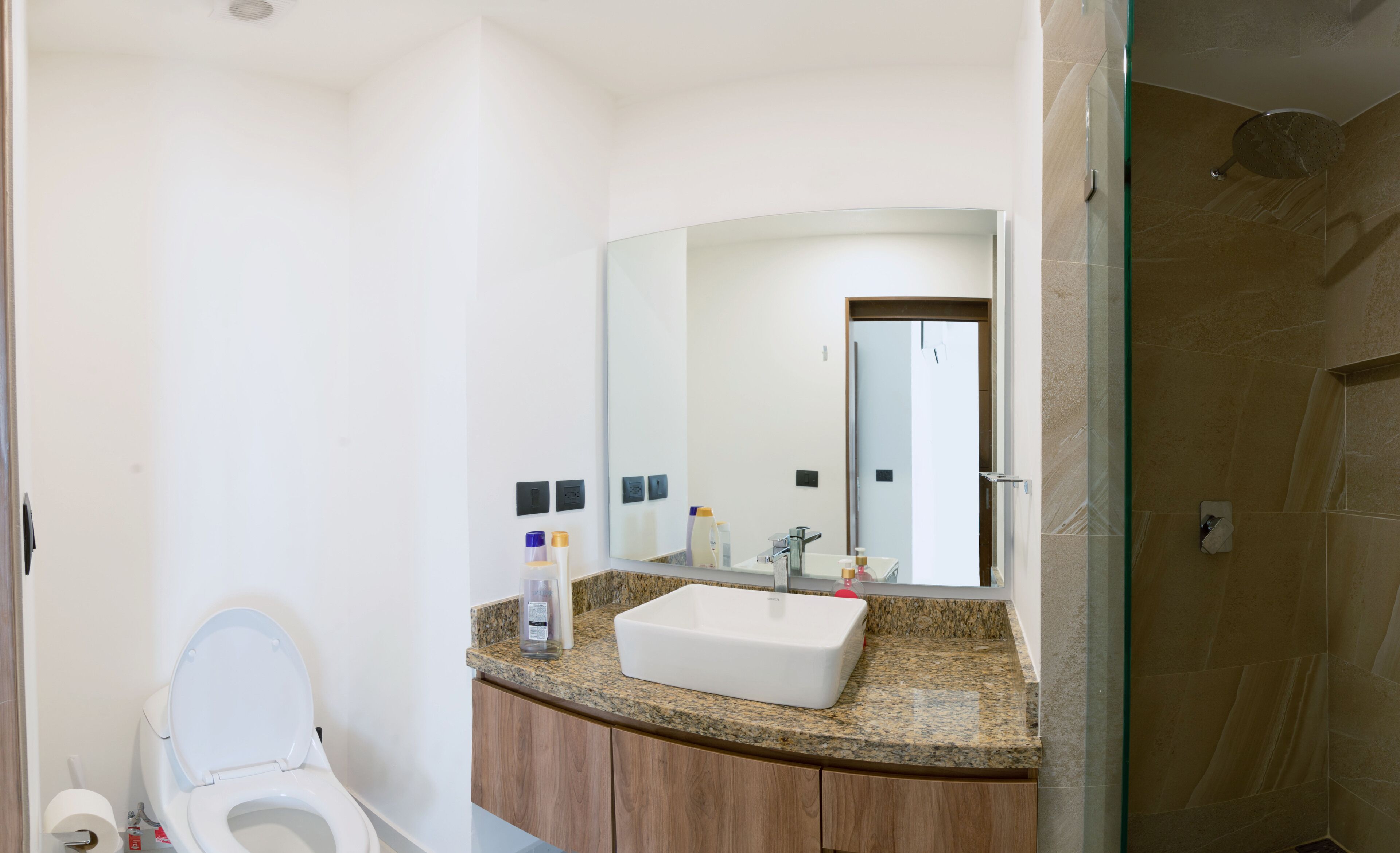 Un baño con inodoro blanco, lavabo con encimera de granito y un espejo grande sobre el lavabo.