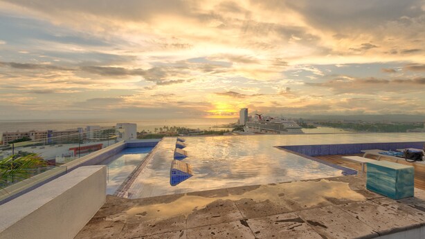 A rooftop pool with a sunset view, a ship in the background, and a cityscape.
