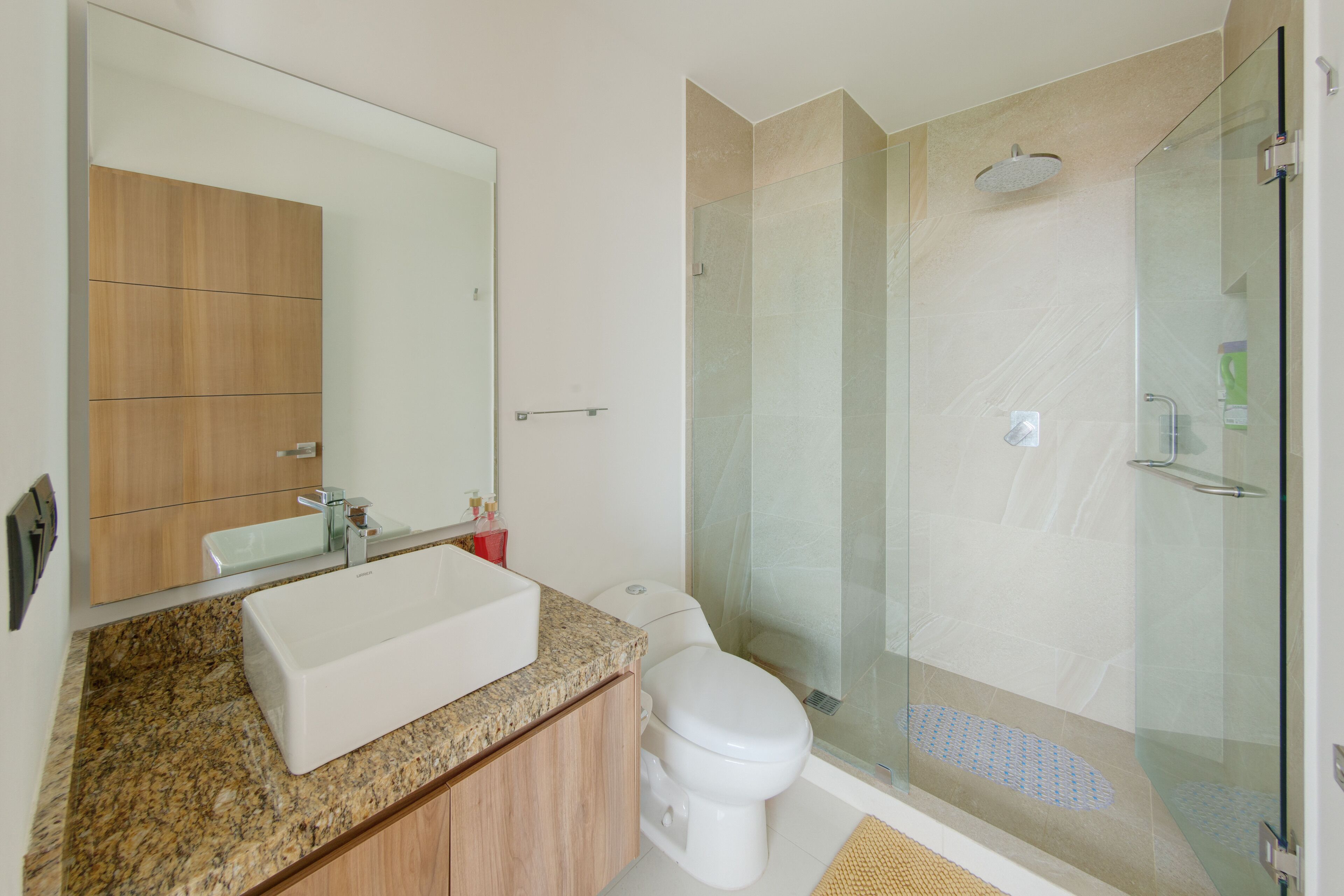 A modern bathroom with a large mirror, a rectangular sink, a toilet, and a glass-enclosed shower area.