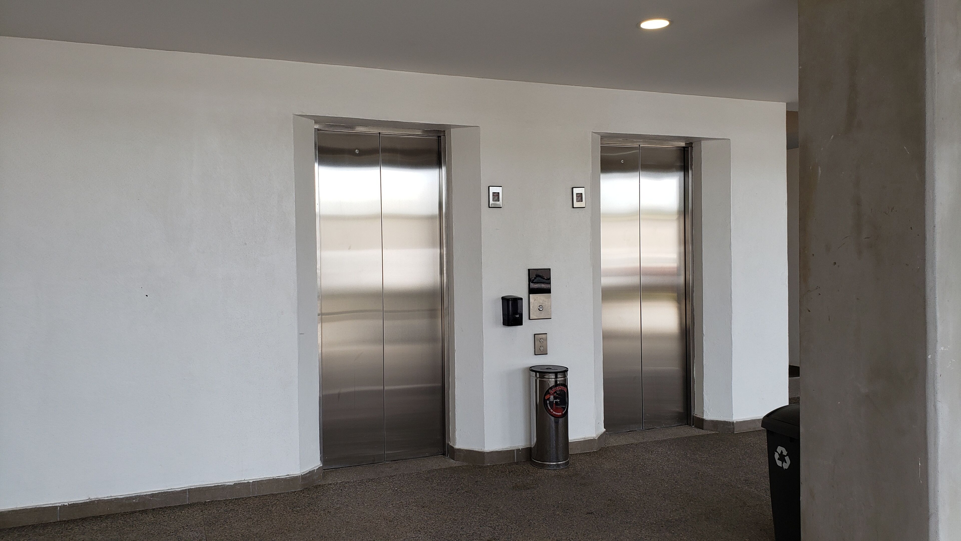 Deux ascenseurs situés dans un couloir, avec une poubelle et un bac de recyclage.