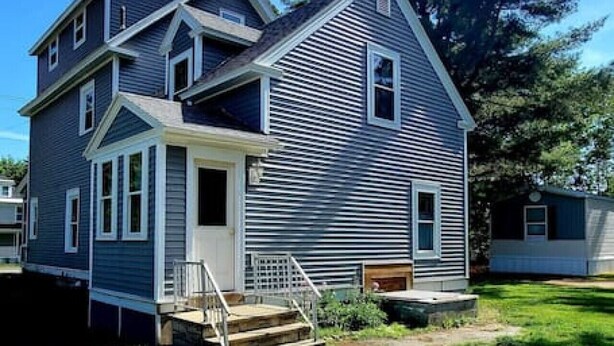 Une maison à deux étages avec un porche à l’avant, un petit garage attenant et une allée menant à la porte d’entrée.
