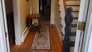 Un couloir doté d’un plancher en bois, d’un tapis, d’un escalier avec une balustrade et d’une porte avec une poignée.
