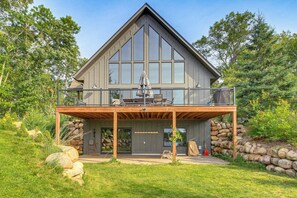 A large, modern two-story house with a prominent balcony, a stone wall, and a well-maintained lawn. - Pequot Lakes Retreat w/ Beach + Fire Pit! (Pequot Lakes)