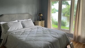 A bedroom with a large bed, a nightstand with a lamp, and a window with curtains. - Welcome to Blueberry Cottage, a peaceful Oasis (Mississippi Mills)