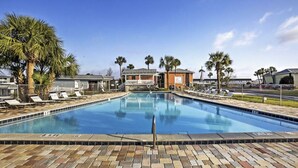 Une piscine avec des chaises longues, des palmiers et un bâtiment en arrière-plan.