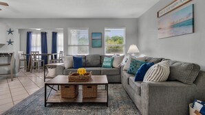 Un salon moderne avec un canapé gris, des coussins bleus, une table basse avec des paniers et un tableau accroché au mur.