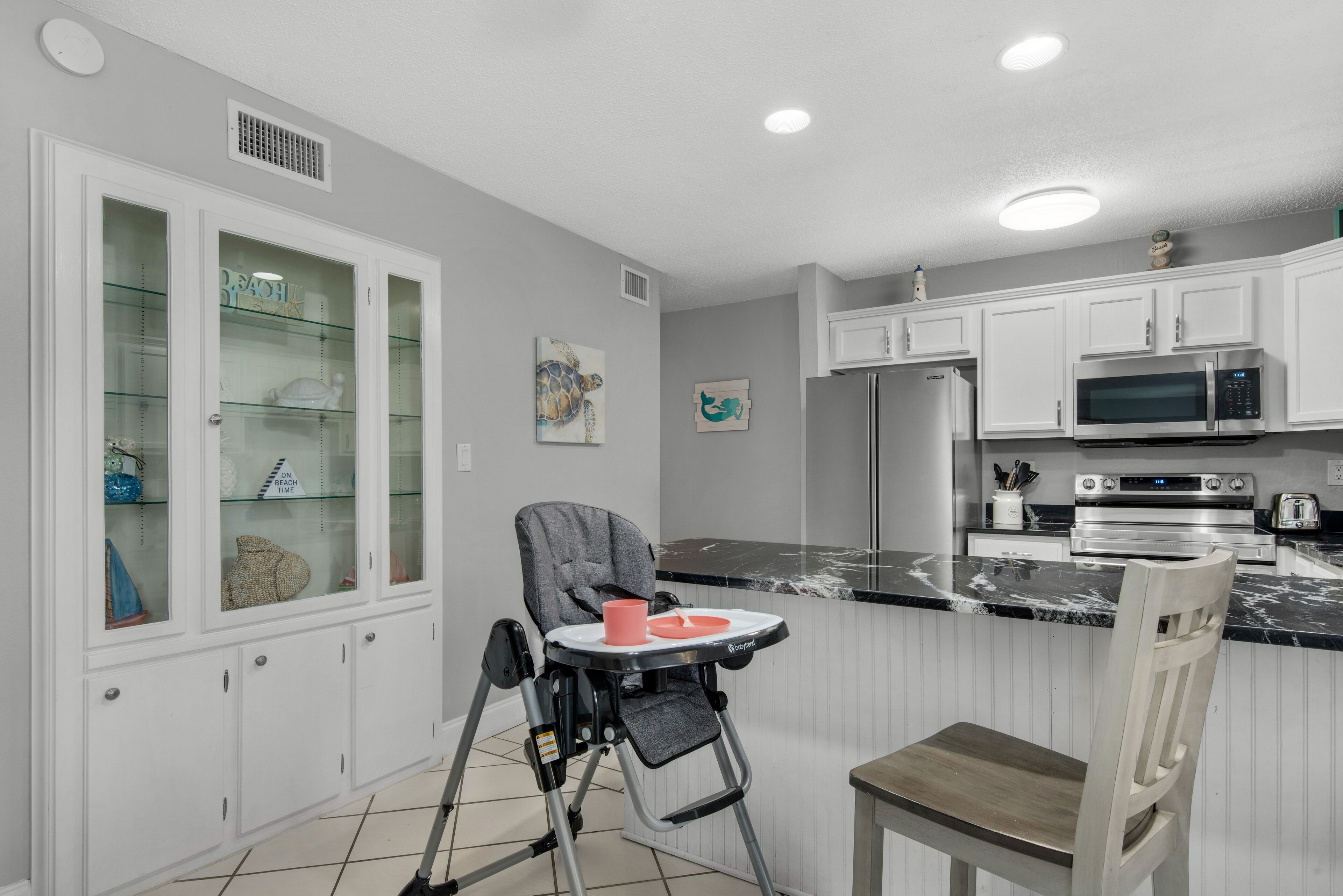 A modern kitchen with white cabinets, a microwave, and a child’s high chair.