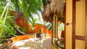 Un espace extérieur ensoleillé doté d’une structure à toit de chaume, d’un hamac et d’un coin salon avec des chaises.