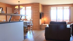 A wooden interior with a dining area, a sofa, and a TV mounted on the wall. - Sunset A 4 by Interhome (Villars)
