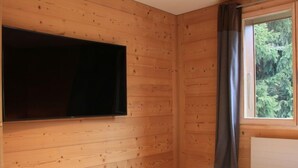A room with wooden walls, a mounted flat-screen TV, a window with curtains, and a bed. - Sunset A 4 by Interhome (Villars)