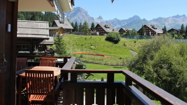 A balcony with wooden railings overlooking a mountainous landscape with traditional wooden houses. - Sunset A 4 by Interhome (Villars)