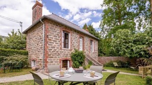 A stone house with a chimney, a round table with chairs, and a small staircase leading to the entrance. - Les Tourelles by Interhome (Dinard)
