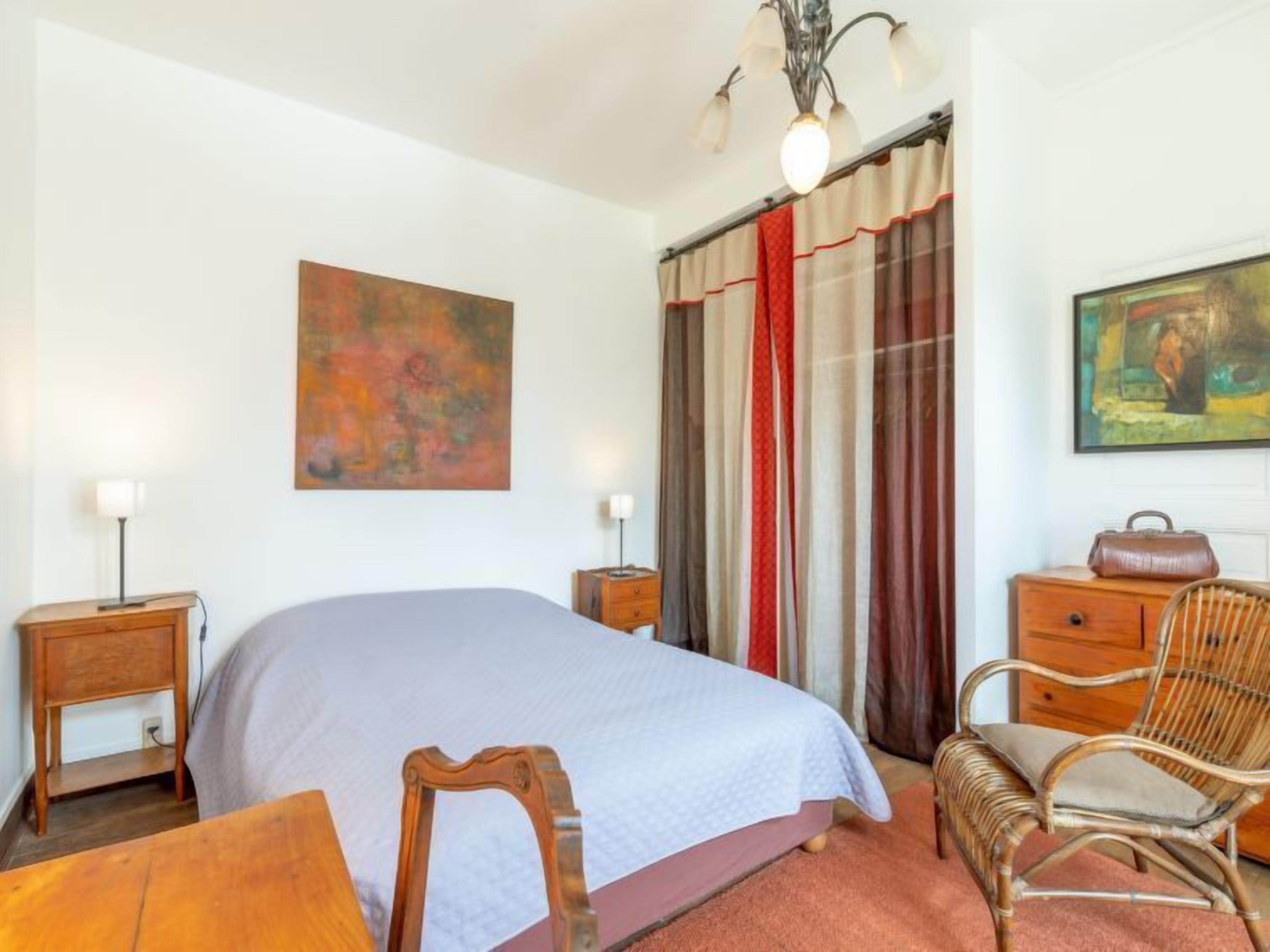 A bedroom with a bed, a chair, a nightstand, a dresser, and a painting on the wall.