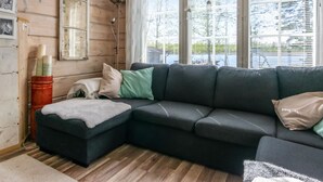 Un cuarto acogedor con un sofá seccional verde oscuro, un pequeño reposapiés y una ventana con persianas.