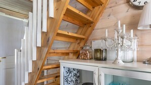 Una escalera de madera en una habitación con un armario blanco que contiene cristalería y un reloj en la pared.