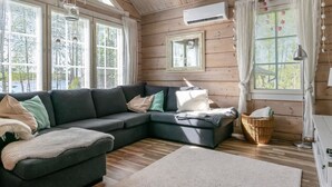 Un interior de cabaña acogedor, con un sofá seccional, un ventanal grande y un ventilador de techo.