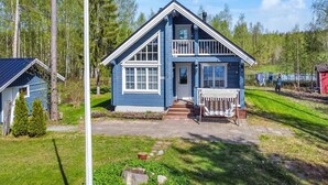 Una casa azul de dos pisos con un balcón, rodeada de árboles y un patio cubierto de césped.
