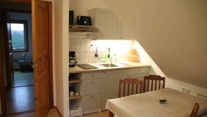 A compact kitchen with a dining area, featuring a wooden table and chairs, a built-in oven, and a window providing natural light. - Scandinavian vacation home with sauna by the Baltic Sea (Stove)