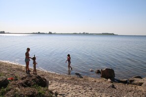 Een strand met een rustige zee, rotsen en een heldere lucht.