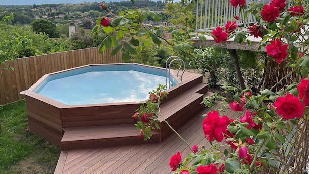 Un bain à remous avec des marches en bois et une terrasse en bois, entouré d’une végétation luxuriante et de fleurs rouges.