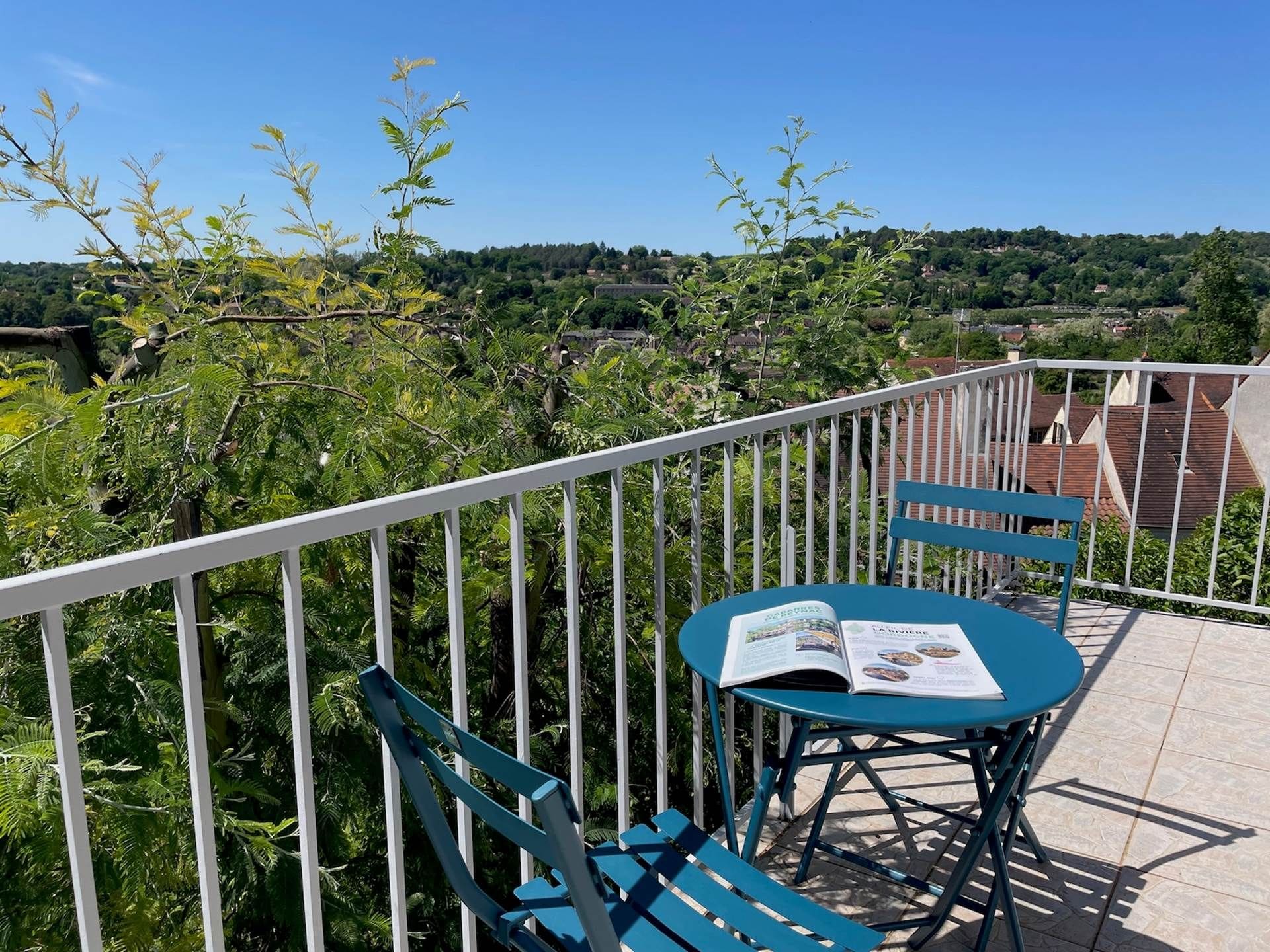 A balcony with a table and chairs, a railing, and a view of a green landscape.