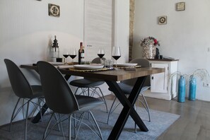 Un coin repas avec une table dressée pour quatre personnes, agrémenté d’une bouteille de vin, de verres et d’un vase rempli de fleurs.