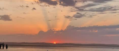 Une plage au coucher du soleil, avec un ciel dégagé, une mer calme et une jetée visible au loin.