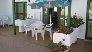Patio esterno con tavolo e sedie, un ombrello blu e piante in vaso.
