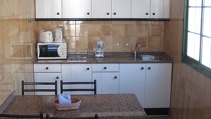 Una cucina compatta con mobili bianchi, un forno a microonde, una macchina da caffè e un lavello. Si nota un tavolo con sedie e un tappeto.