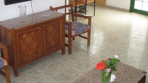 Zona pranzo con tavolo in granito, sedie in legno, televisione a parete e finestra con vista sul verde.