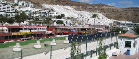 A coastal resort with white buildings, a swimming pool, and a fenced area with plants and inflatable rings.