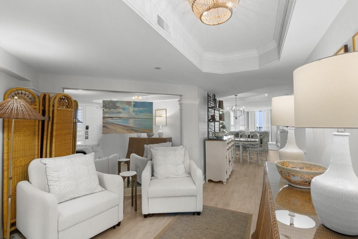 A spacious living area with white furniture, a dining area, and a kitchen.