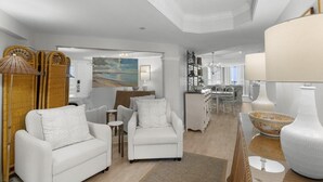A spacious living area with white furniture, a dining area, and a kitchen.