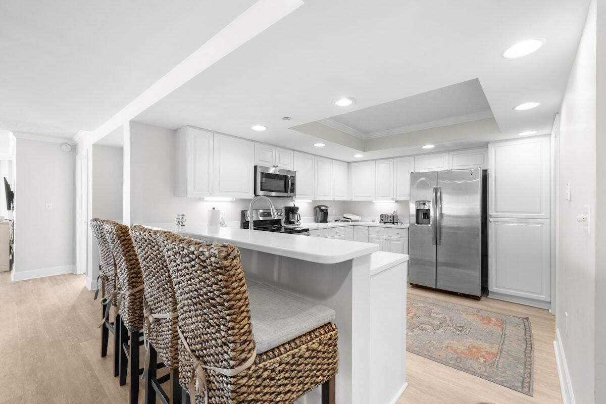 A modern kitchen with white cabinetry, a central island, and a seating area with woven chairs.