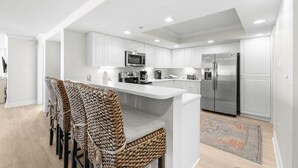 A modern kitchen with white cabinetry, a central island, and a seating area with woven chairs.