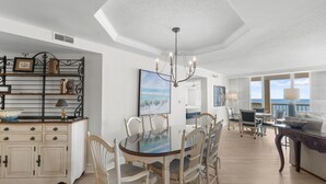 A dining area with a round table, chairs, a chandelier, and a view of the ocean.