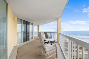 A balcony with a view of the ocean, a chair, and a table.