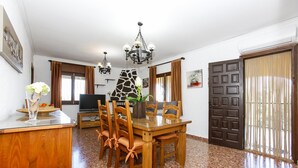 A dining area with a wooden table and chairs, a chandelier, and a stone fireplace. - 014 Villa Colonia (Denia)