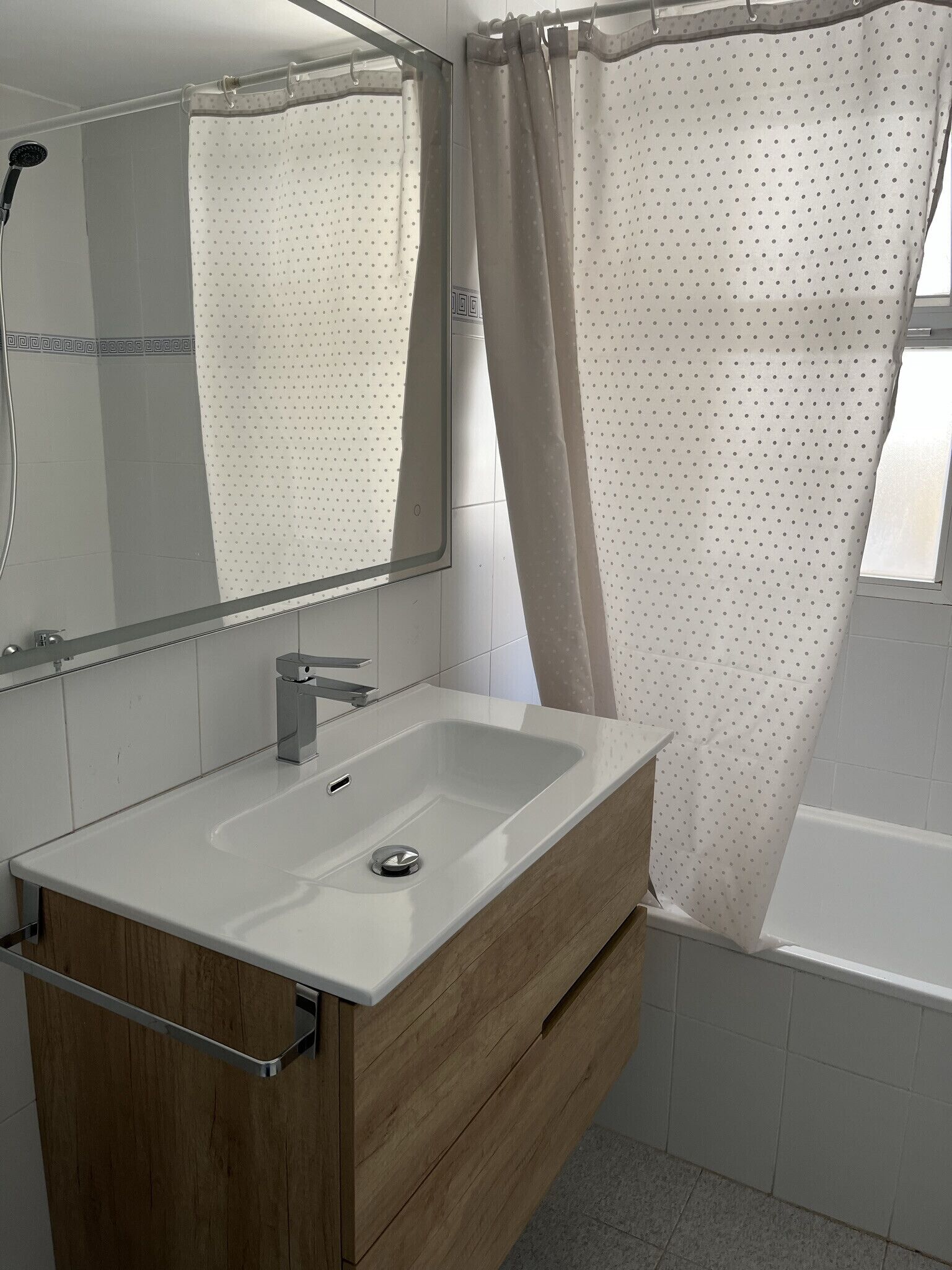 Ein modernes Badezimmer mit einem weißen Waschbecken, einem Holz-Waschtisch, einem Spiegel und einer Duschvorhang.