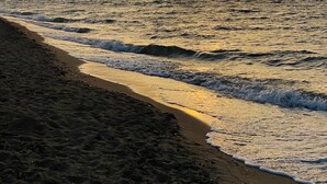 Una playa con olas, un atardecer y montañas a lo lejos.