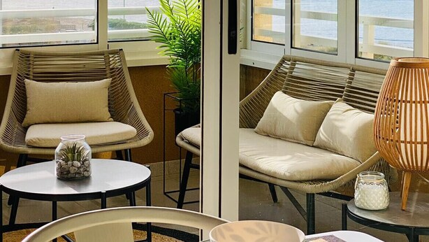 Una habitación con vista al mar, dos sillas de mimbre, una mesa con un cuenco y una planta en maceta.