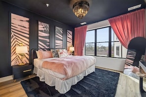 A bedroom with a bed, a nightstand, a mirror, a window with curtains, and a chandelier.