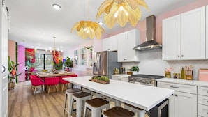 A modern kitchen with white cabinets, a central island, bar stools, and a dining area with a red table and chairs.