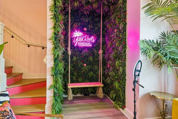 A staircase with a neon sign reading 'Wild Roots Nashville Tennessee' and a swing hanging from the wall.